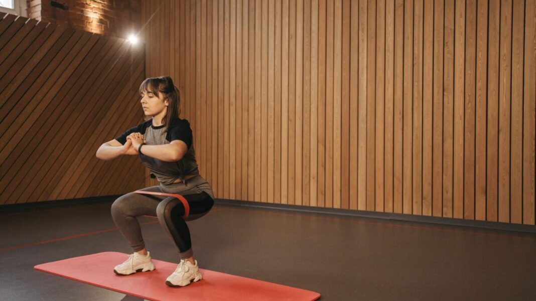 Young woman exercises indoors with resistance band on mat for fitness