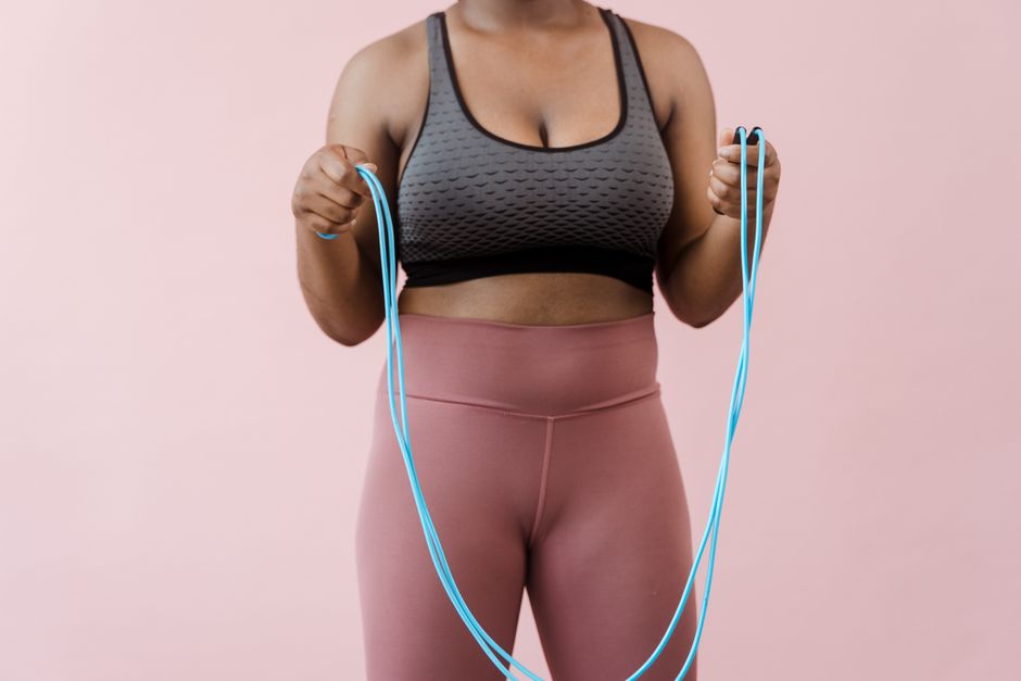 Close-up of a woman in activewear holding a jump rope against a pink background.